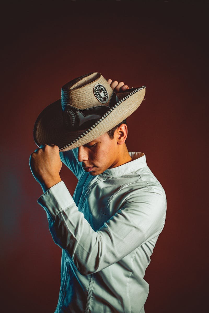 A man in traditional Mexican attire with a cowboy hat poses against a dark background.