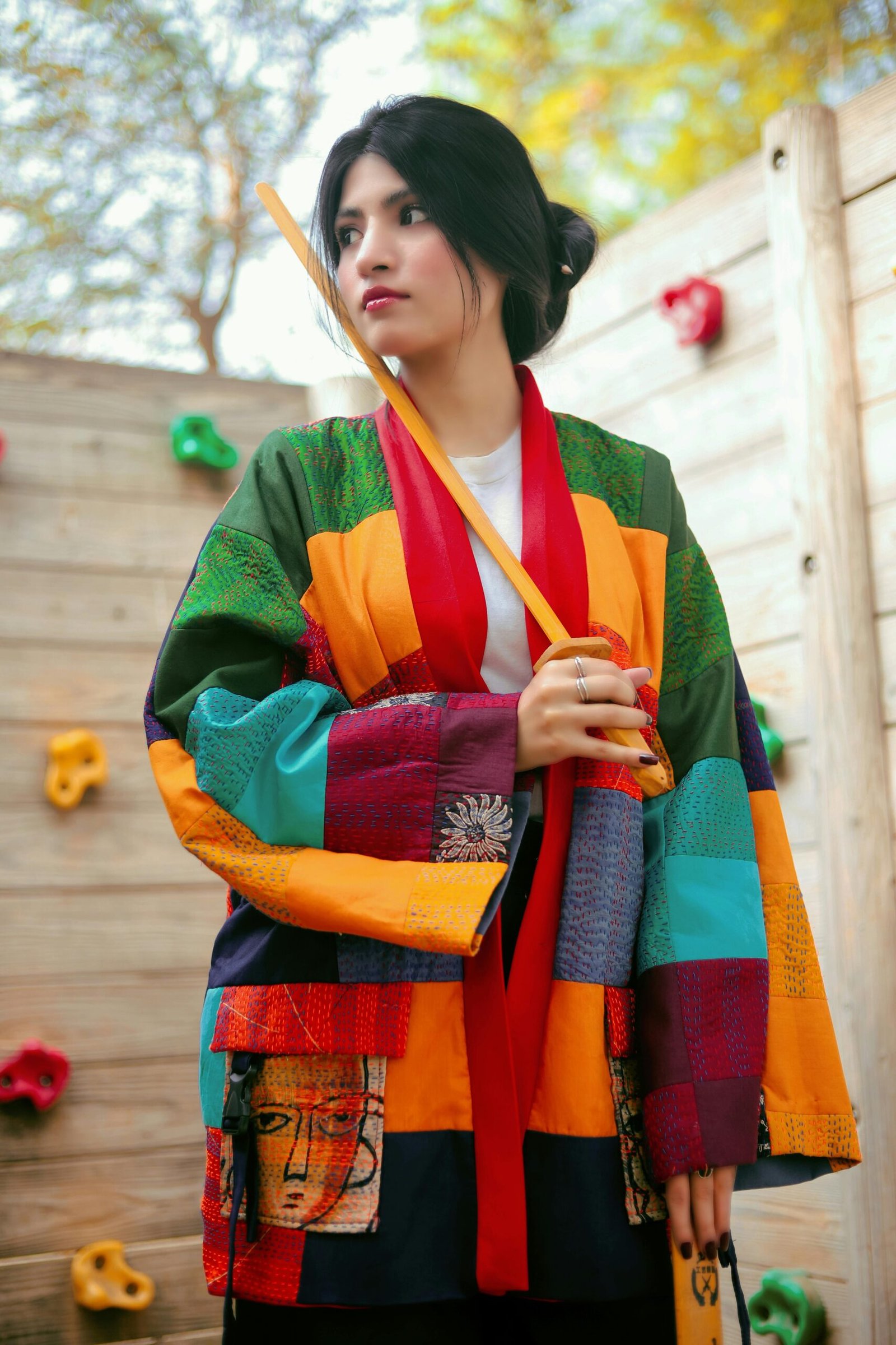 Stylish portrait of a woman in colorful kimono holding a bokken, showcasing unique fashion in a serene setting.